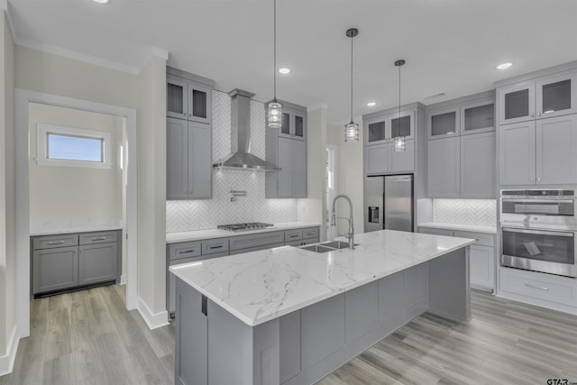 kitchen with a kitchen island with sink, sink, wall chimney range hood, and appliances with stainless steel finishes