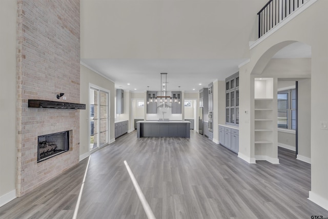 unfurnished living room featuring a brick fireplace, crown molding, and light wood-type flooring