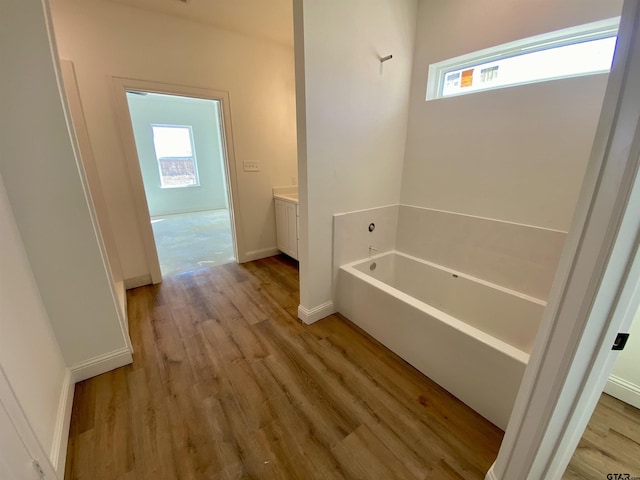 full bath with vanity, a bath, wood finished floors, and baseboards