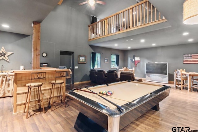 game room with a high ceiling, pool table, bar, and light hardwood / wood-style floors