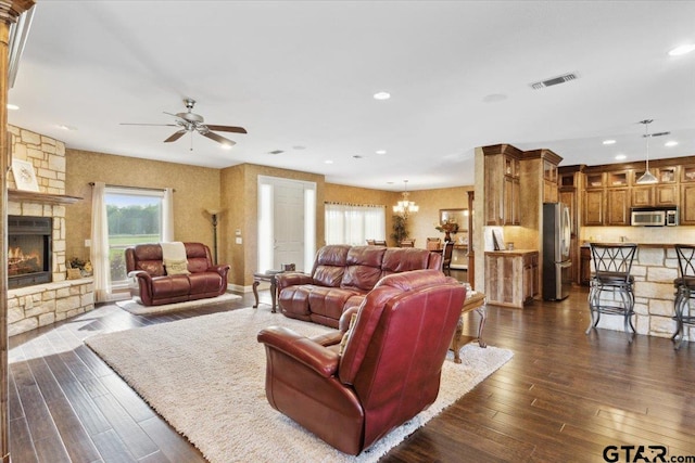 living room with ceiling fan with notable chandelier, dark hardwood / wood-style floors, and a fireplace