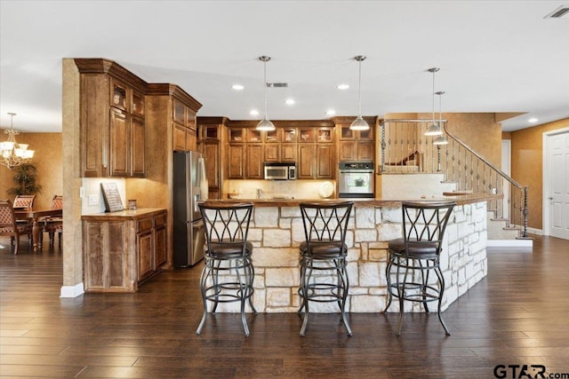 kitchen with dark hardwood / wood-style flooring, an inviting chandelier, a kitchen breakfast bar, pendant lighting, and appliances with stainless steel finishes