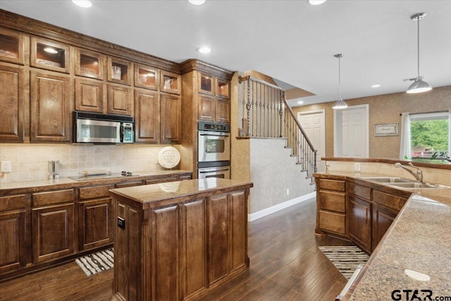 kitchen with dark hardwood / wood-style flooring, a center island, hanging light fixtures, light stone countertops, and appliances with stainless steel finishes