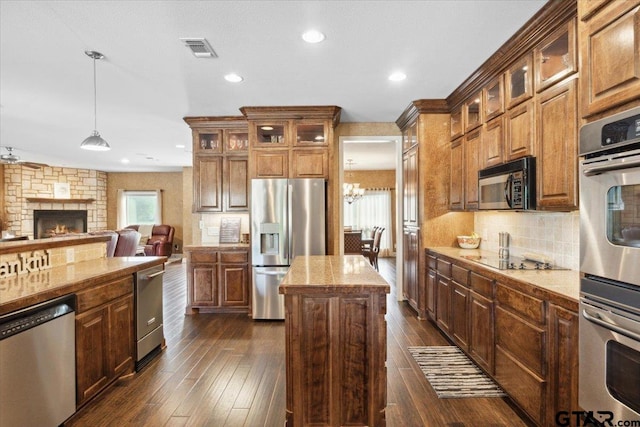 kitchen with a stone fireplace, stainless steel appliances, dark hardwood / wood-style floors, a kitchen island, and decorative light fixtures