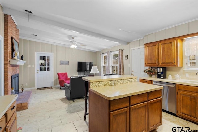 kitchen featuring stainless steel dishwasher, ceiling fan, a fireplace, beamed ceiling, and a kitchen island