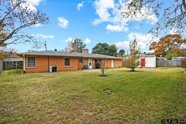 back of property with central air condition unit, a yard, and a storage shed