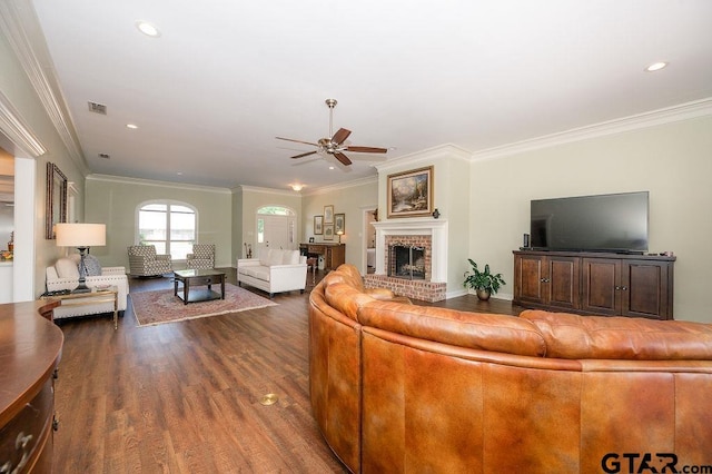 living area featuring wood finished floors, a ceiling fan, visible vents, crown molding, and a brick fireplace