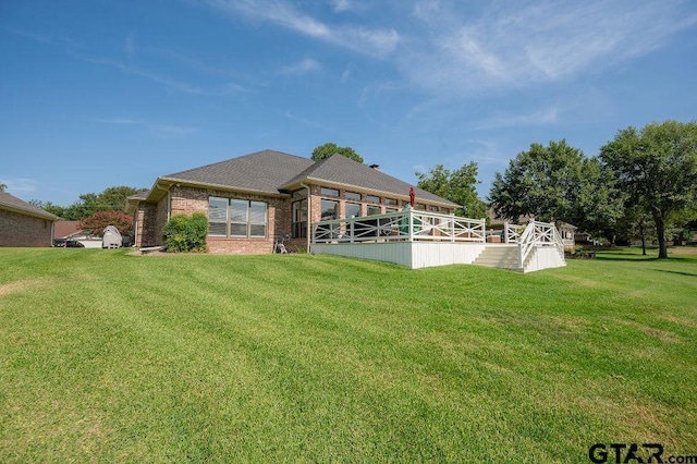 back of property featuring brick siding, a shingled roof, and a yard