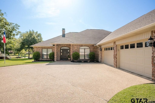 view of front of home with driveway, roof with shingles, an attached garage, a chimney, and brick siding