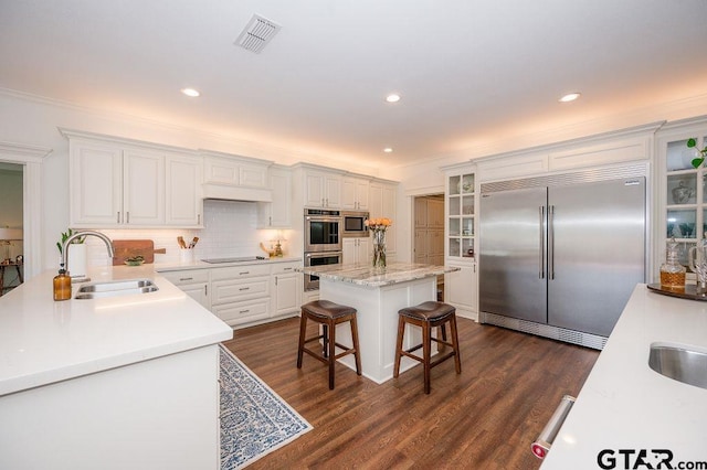 kitchen with visible vents, dark wood finished floors, built in appliances, a breakfast bar, and a sink