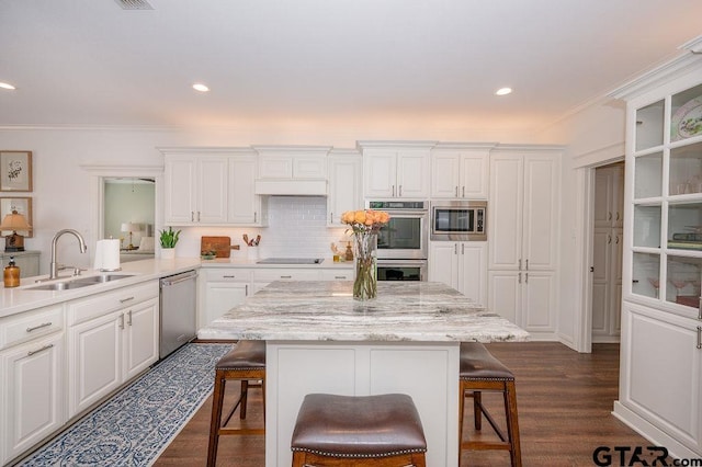 kitchen with decorative backsplash, a kitchen breakfast bar, white cabinets, stainless steel appliances, and a sink