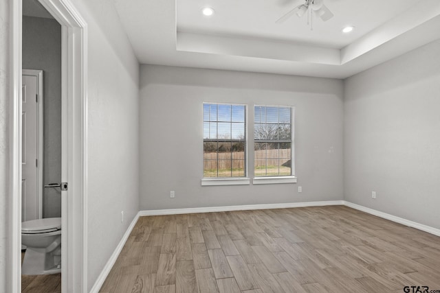 interior space featuring connected bathroom, a tray ceiling, ceiling fan, and light hardwood / wood-style floors