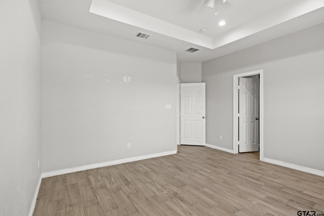 unfurnished room with a raised ceiling, ceiling fan, and light wood-type flooring