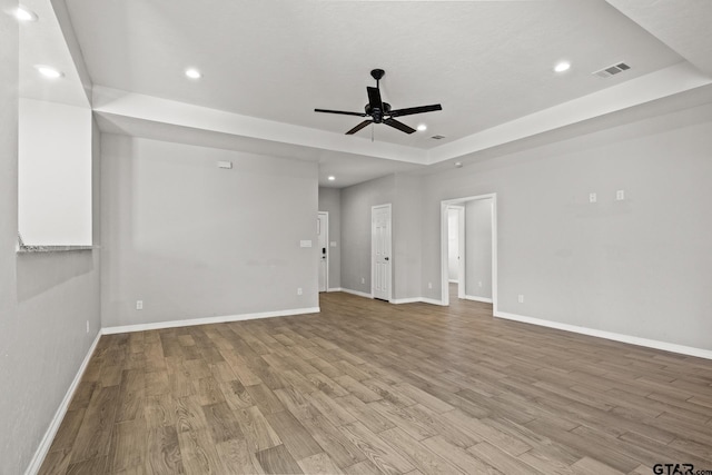 empty room featuring a raised ceiling, ceiling fan, and light hardwood / wood-style floors