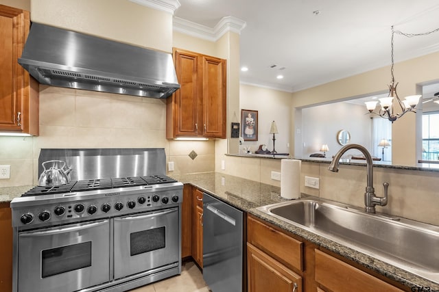 kitchen featuring tasteful backsplash, stainless steel appliances, dark stone counters, wall chimney range hood, and an inviting chandelier