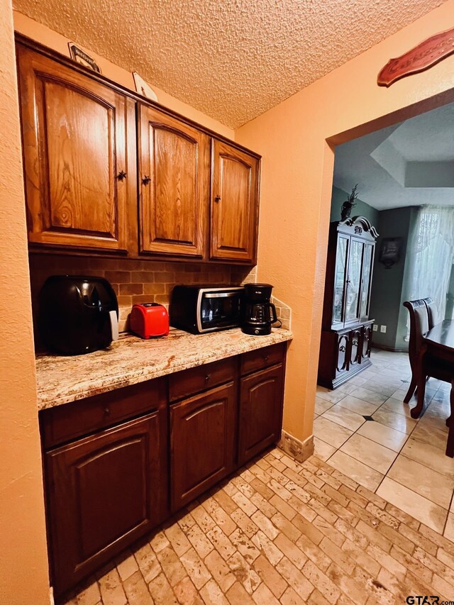 2000 Homestead Dr, Mesquite, TX 75181 - kitchen with backsplash, a textured ceiling, brown cabinets, and light stone counters