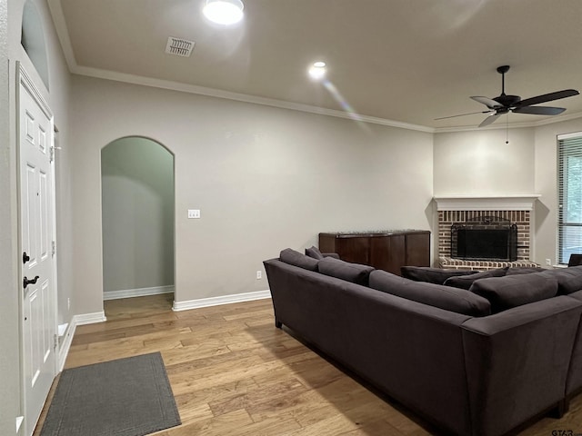 2509 Guinn Farms Rd, Tyler, TX 75707 - living room with arched walkways, a ceiling fan, ornamental molding, light wood-type flooring, and a brick fireplace