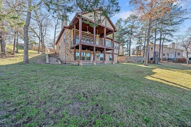 back of property with ceiling fan, a balcony, and a yard