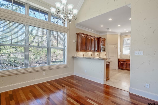 kitchen with light stone counters, ornamental molding, a chandelier, hardwood / wood-style floors, and stainless steel microwave