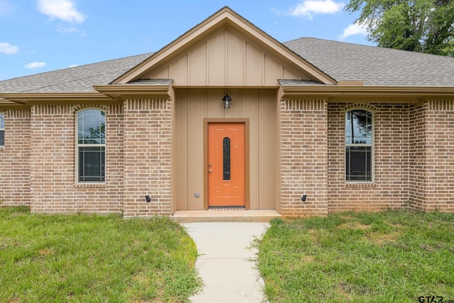 view of front of house featuring a shingled roof, a front yard, brick siding, and board and batten siding