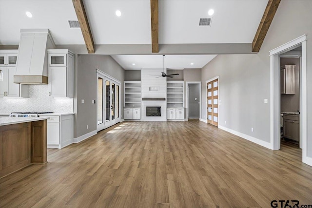 unfurnished living room featuring beamed ceiling, a large fireplace, ceiling fan, and light wood-type flooring