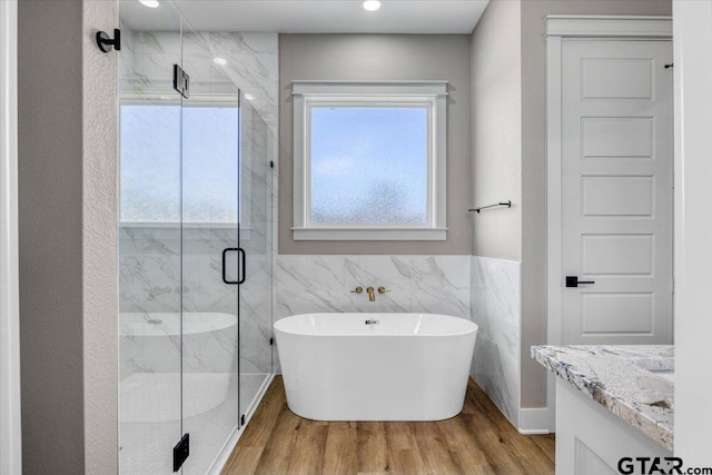 bathroom with vanity, independent shower and bath, hardwood / wood-style floors, and tile walls