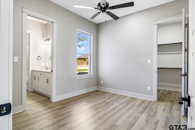 unfurnished bedroom with a spacious closet, ensuite bath, a closet, and light wood-type flooring