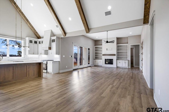 unfurnished living room with high vaulted ceiling, a large fireplace, hardwood / wood-style flooring, ceiling fan, and beam ceiling