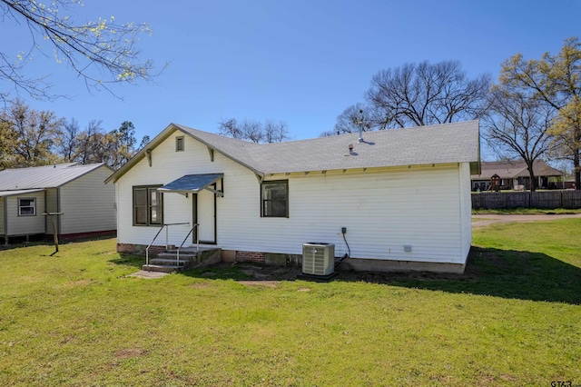 rear view of house featuring a yard, central air condition unit, a shingled roof, and entry steps
