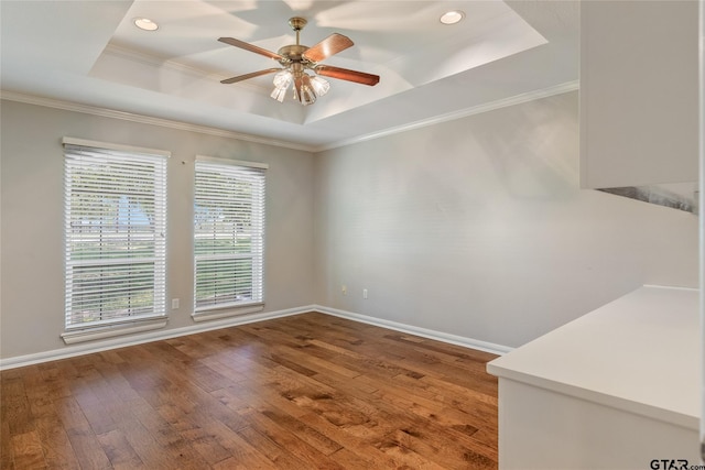 empty room featuring hardwood / wood-style floors, a raised ceiling, a healthy amount of sunlight, and crown molding