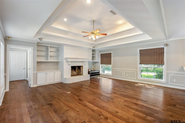 unfurnished living room with a fireplace, a tray ceiling, built in features, and dark wood-type flooring