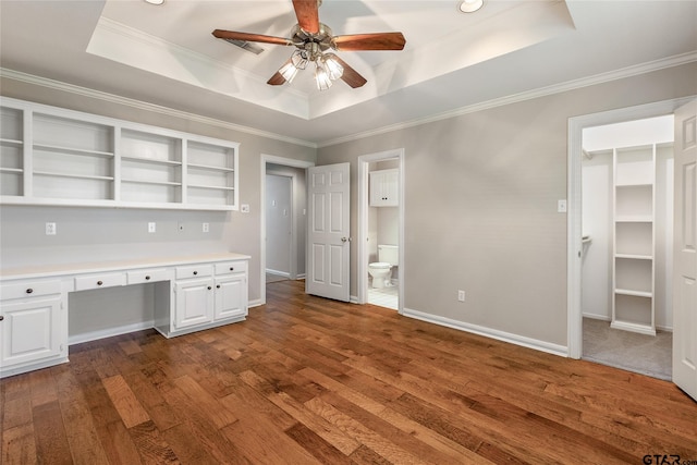 unfurnished office featuring built in desk, dark hardwood / wood-style floors, a raised ceiling, and ceiling fan