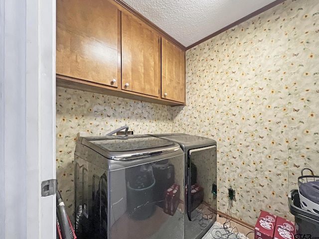 clothes washing area featuring cabinet space, wallpapered walls, washing machine and clothes dryer, crown molding, and a textured ceiling