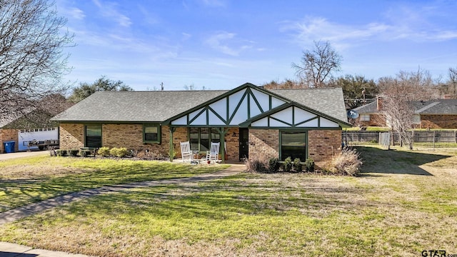 view of front of home featuring brick siding, roof with shingles, a front yard, and fence