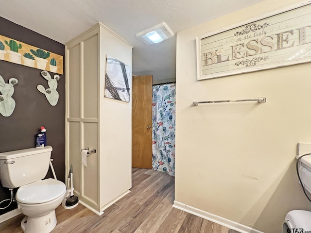 bathroom featuring toilet, a textured ceiling, baseboards, and wood finished floors