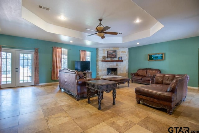 living room featuring a stone fireplace, french doors, ceiling fan, and a raised ceiling