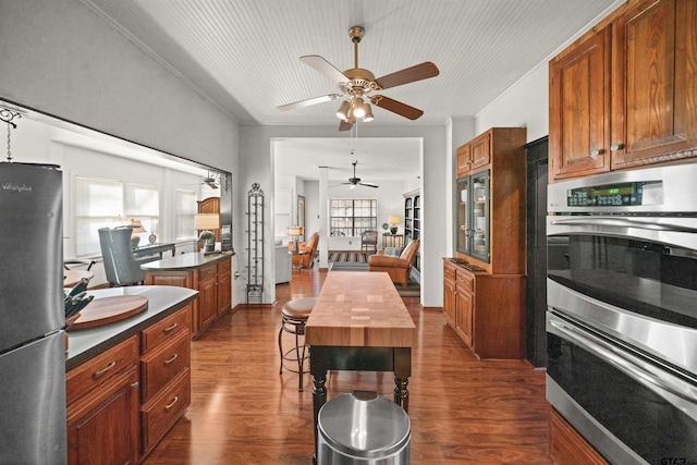 kitchen featuring a ceiling fan, appliances with stainless steel finishes, brown cabinetry, and dark wood-type flooring