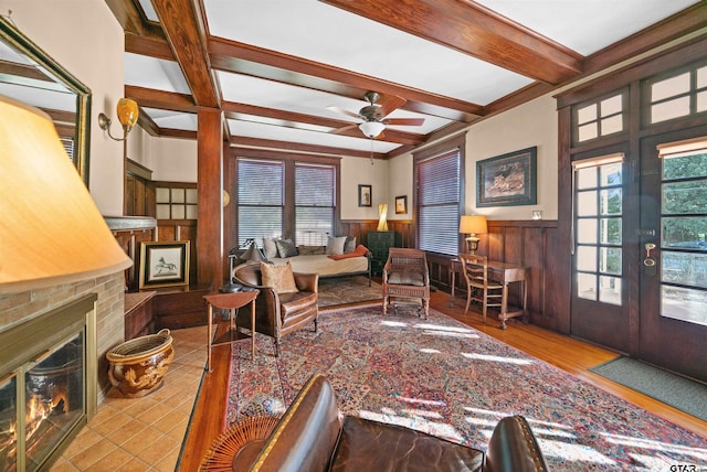 living room featuring wainscoting, a brick fireplace, beamed ceiling, ceiling fan, and coffered ceiling
