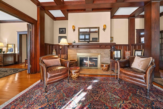 living room featuring wood finished floors, beam ceiling, a fireplace, a wainscoted wall, and coffered ceiling