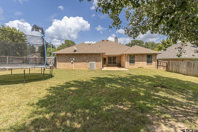 rear view of house with central AC, a patio, a yard, and a trampoline