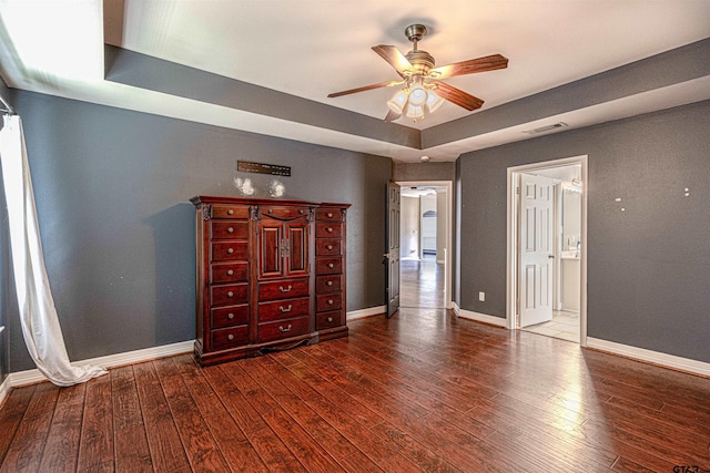 unfurnished bedroom featuring a raised ceiling, ceiling fan, and dark hardwood / wood-style flooring