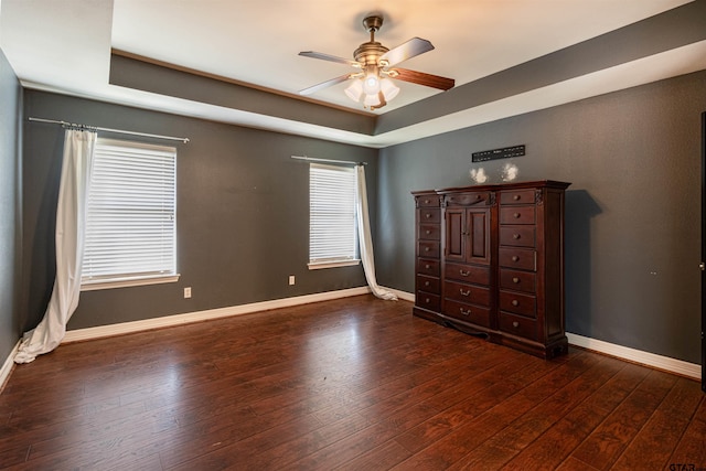 unfurnished bedroom with a raised ceiling, dark wood-type flooring, and ceiling fan