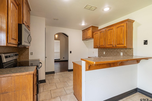 kitchen with appliances with stainless steel finishes, a breakfast bar area, backsplash, light tile patterned floors, and kitchen peninsula