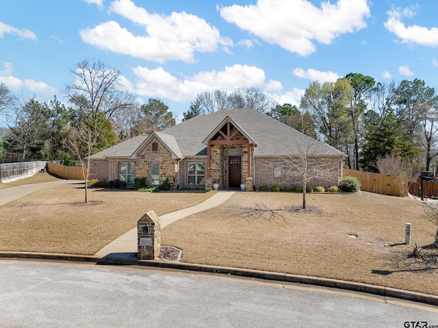 view of front of home with brick siding, a shingled roof, and fence