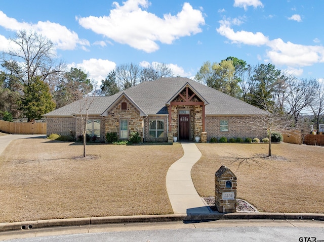 view of front facade with stone siding, a shingled roof, and fence