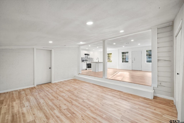 unfurnished living room with light hardwood / wood-style flooring, brick wall, a textured ceiling, and sink