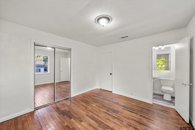 unfurnished bedroom with multiple windows, ensuite bath, dark hardwood / wood-style floors, and a closet