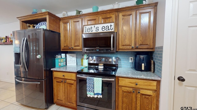 kitchen featuring stainless steel appliances, light tile patterned flooring, light stone counters, and decorative backsplash