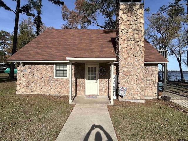 view of front of home featuring a shingled roof, fence, stone siding, a chimney, and a front yard