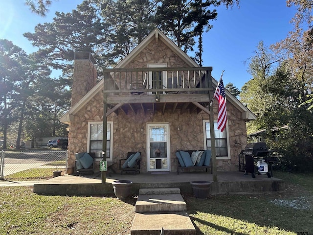 view of front of house with a balcony, stone siding, a patio area, and a chimney